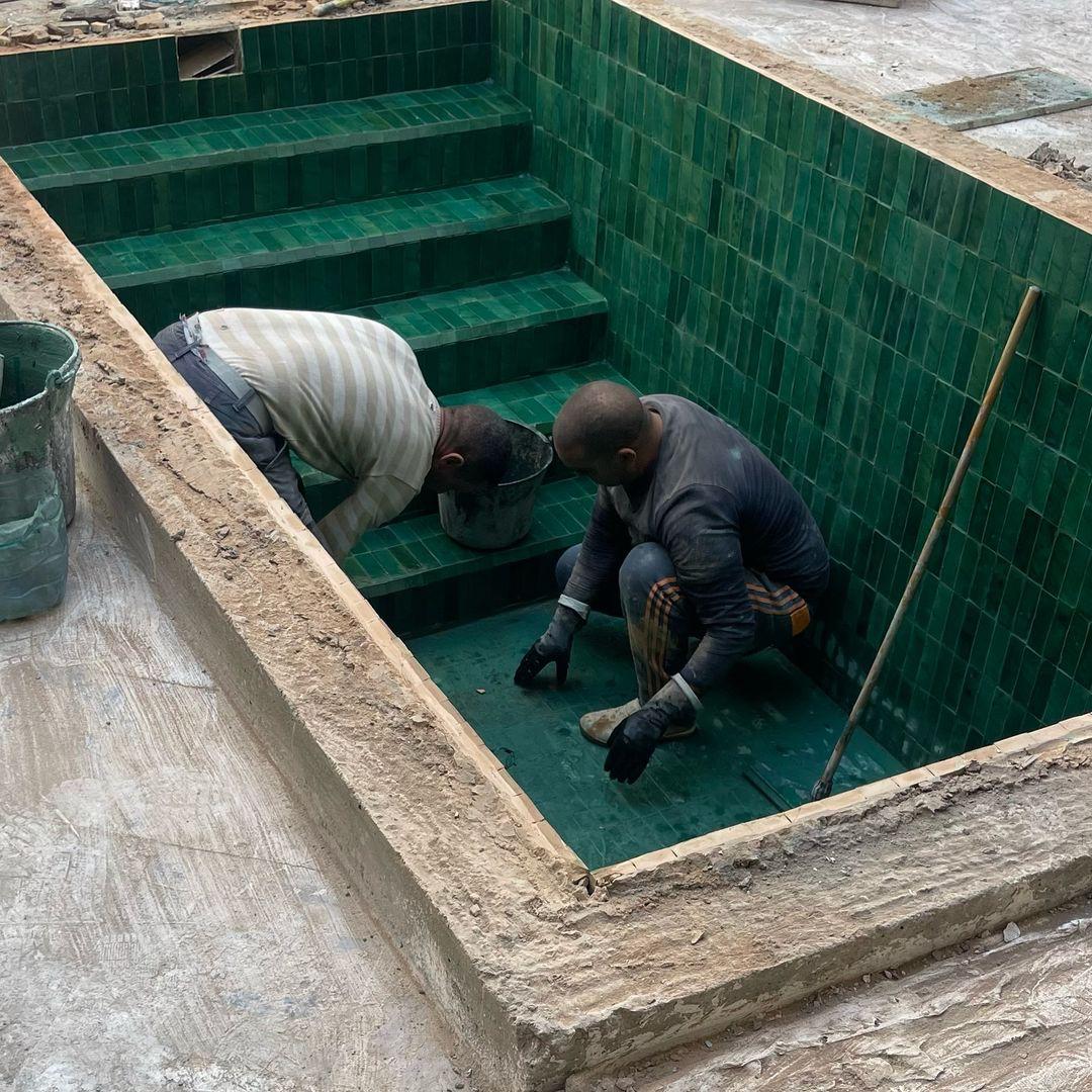 Artisans laying green zellige tiles in a pool